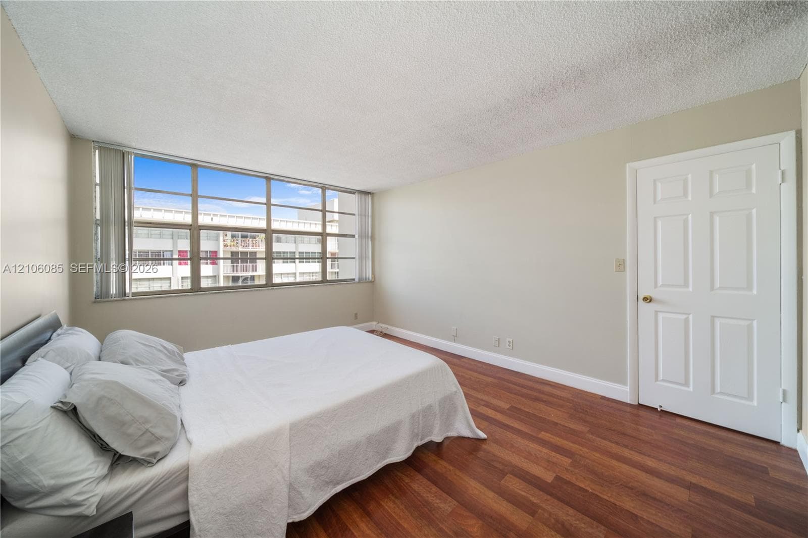 Interior room featuring expansive windows with vertical blinds, wood-finish flooring, and a six-panel door