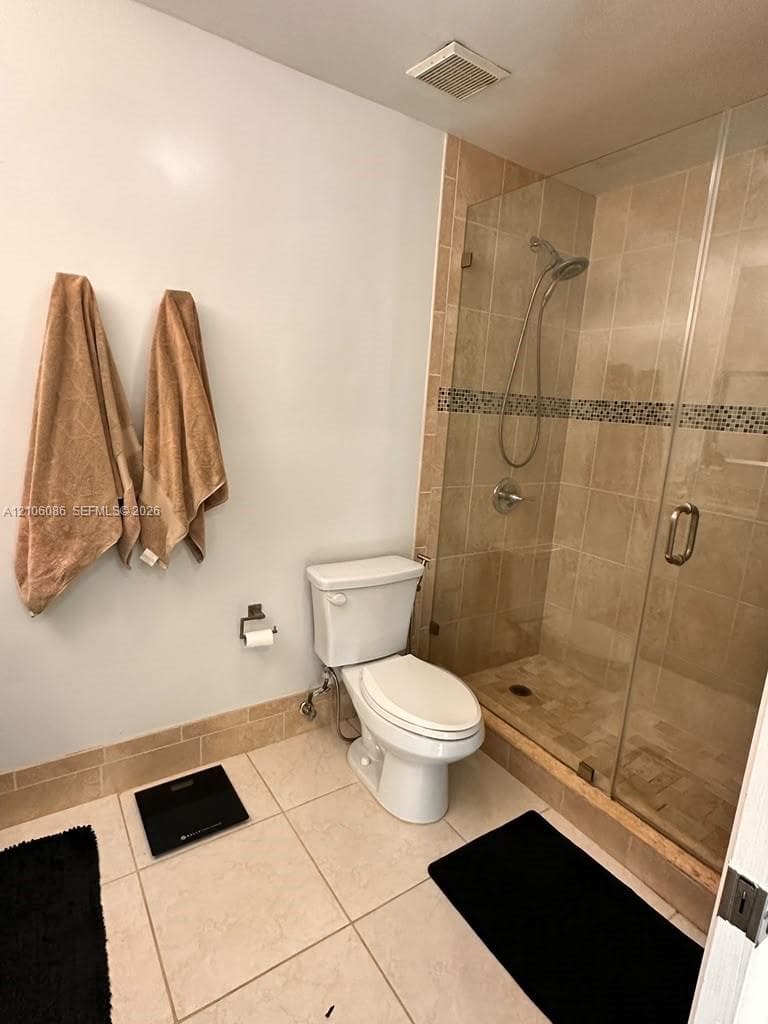 Walk-in glass-enclosed shower featuring neutral-toned wall tiling, decorative mosaic tile accents, and large-format floor tile throughout