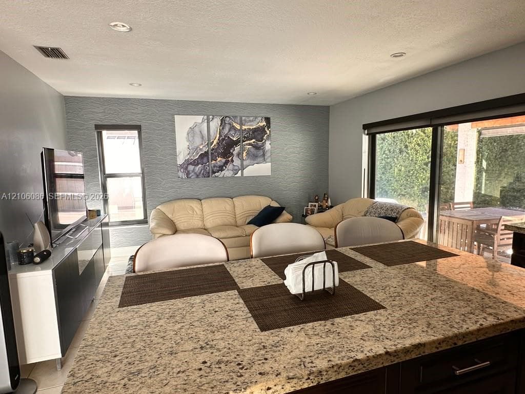 Kitchen island with stone countertop, textured accent wall, recessed lighting, tile flooring, and large sliding glass door