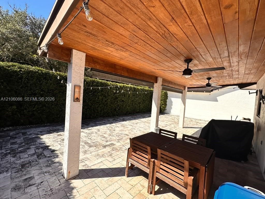 Covered patio featuring a wood-plank ceiling, structural support columns, ceiling fans, and stone-paver flooring