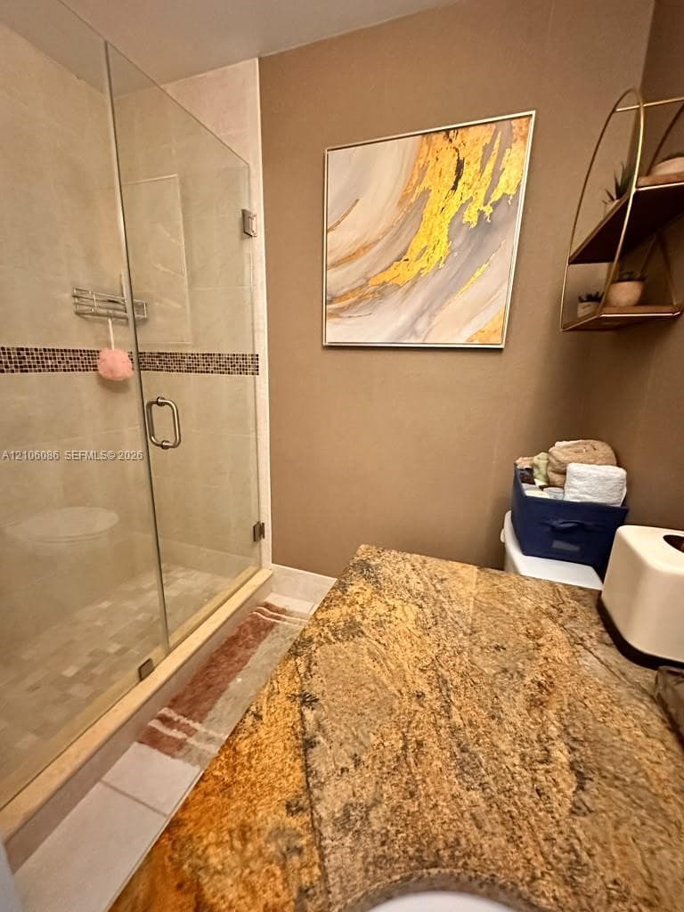 Glass-enclosed shower with tiled walls and a decorative mosaic border, complemented by a stone-surfaced vanity
