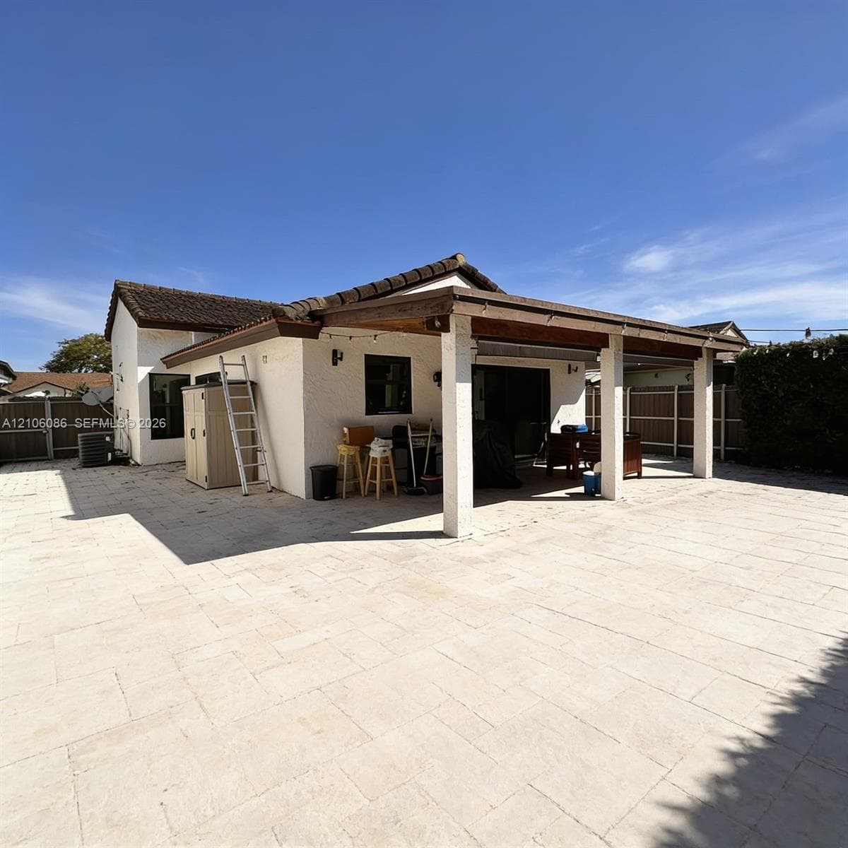 Stucco exterior featuring an expansive paved patio and a covered outdoor living area with wood-beam ceiling supports and perimeter fencing