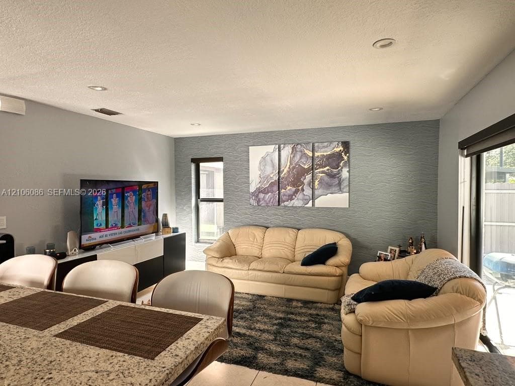 Neutral-toned interior featuring recessed lighting, a textured accent wall, and stone-surface kitchen island