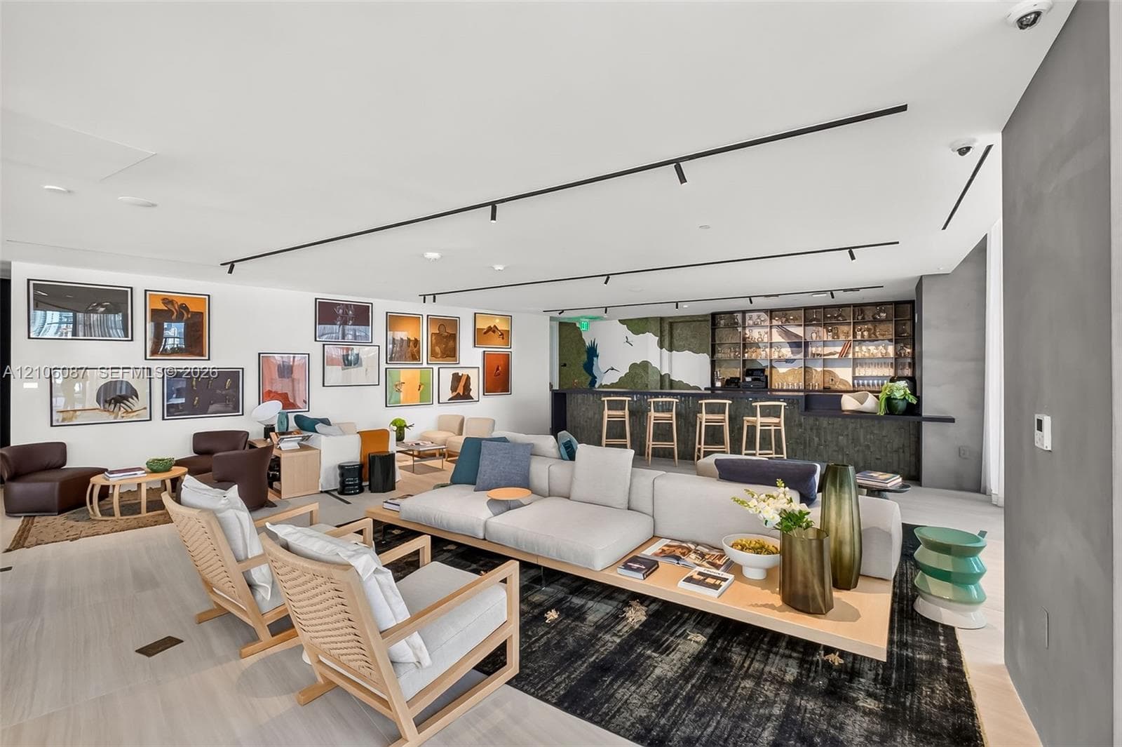 Open-concept space featuring light-toned wood-finish flooring, recessed track lighting, a built-in wet bar with dark stone-finish facing, and decorative glass shelving