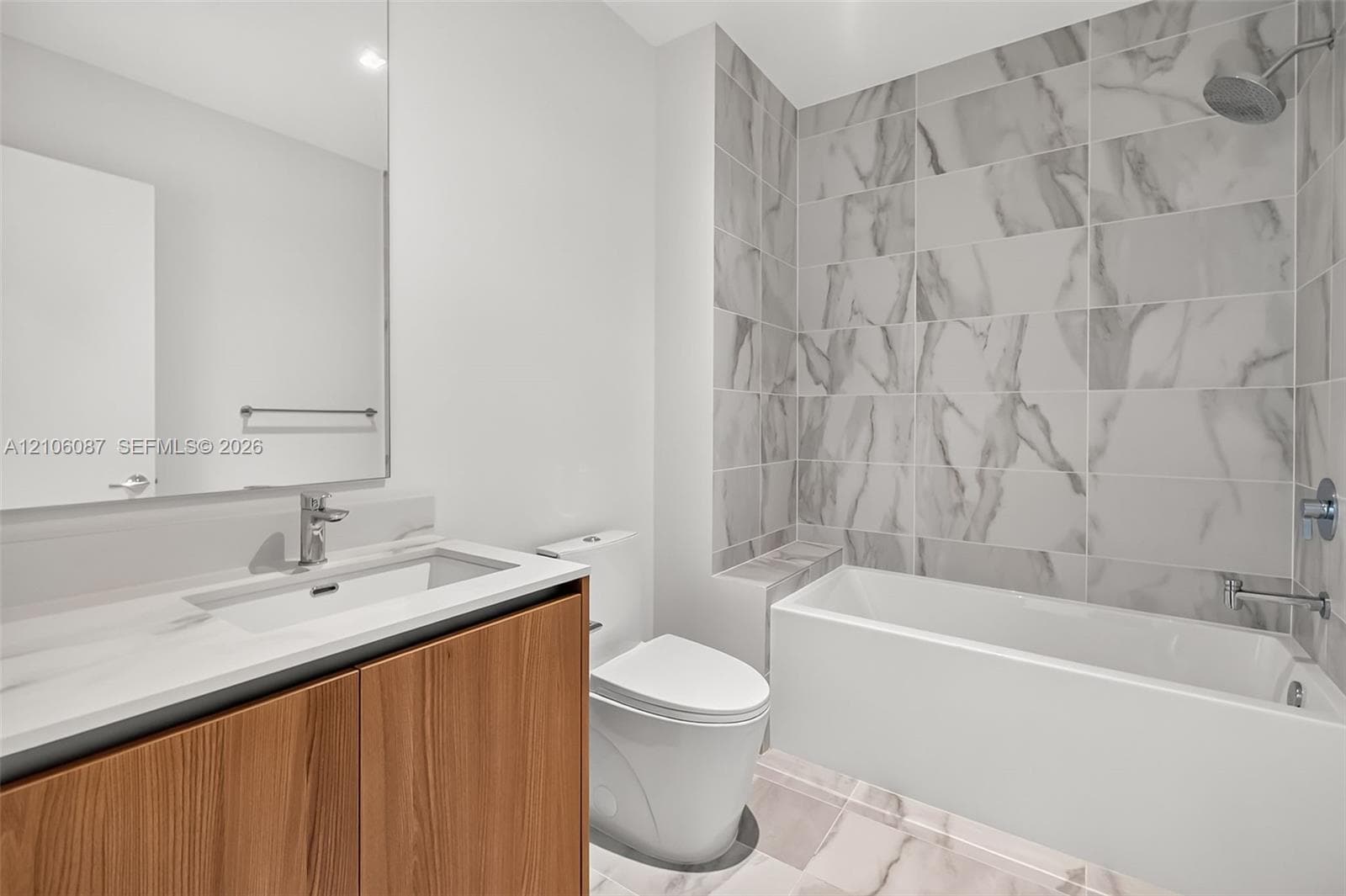 Wood-finish cabinetry, rectangular under-mount sink, stone-composite countertop, full-width mirror, and shower-tub combination with large-format tile surround
