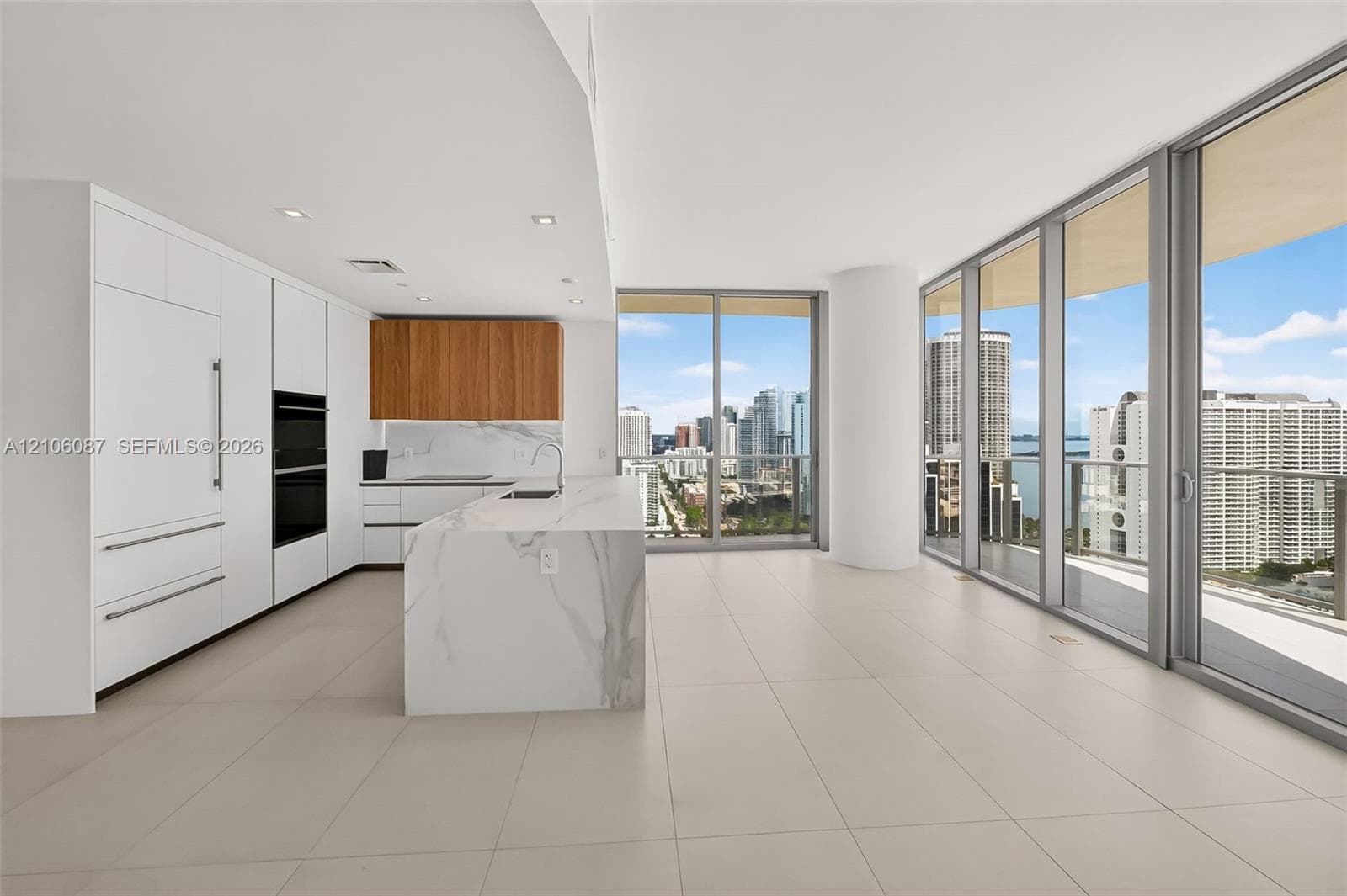 Kitchen featuring floor-to-ceiling cabinetry, a stone-surface island with waterfall edge, integrated appliances, wood-finish upper cabinets, and expansive glass walls