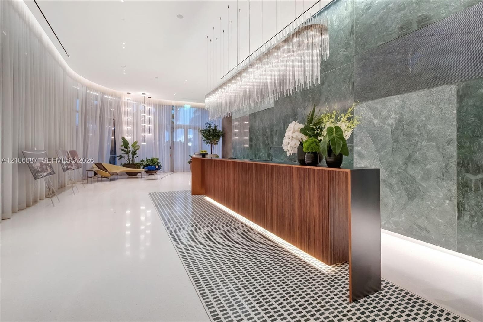 Reception area featuring a wood-panel console, large-format green stone wall cladding, custom crystal-style pendant lighting, polished white flooring, and inset mosaic floor detailing