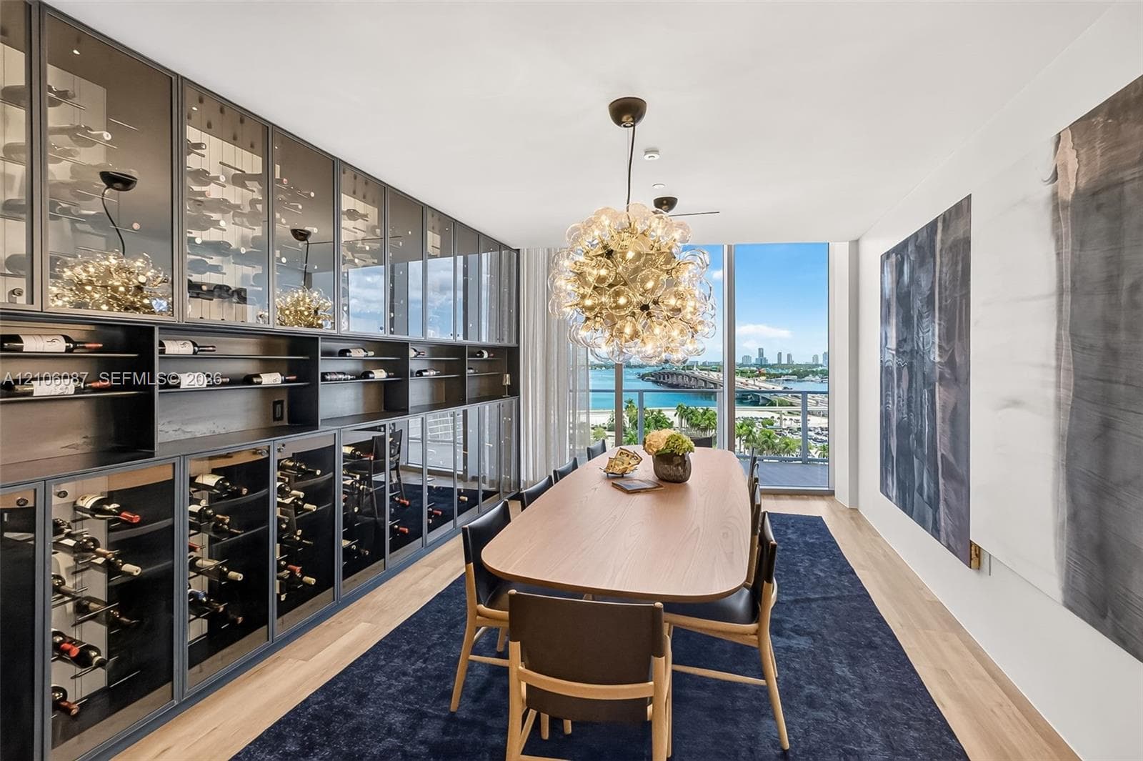 Custom floor-to-ceiling glass-front wine cabinetry, expansive floor-to-ceiling windows, spherical multi-bulb pendant lighting, and light-toned wood-finish flooring