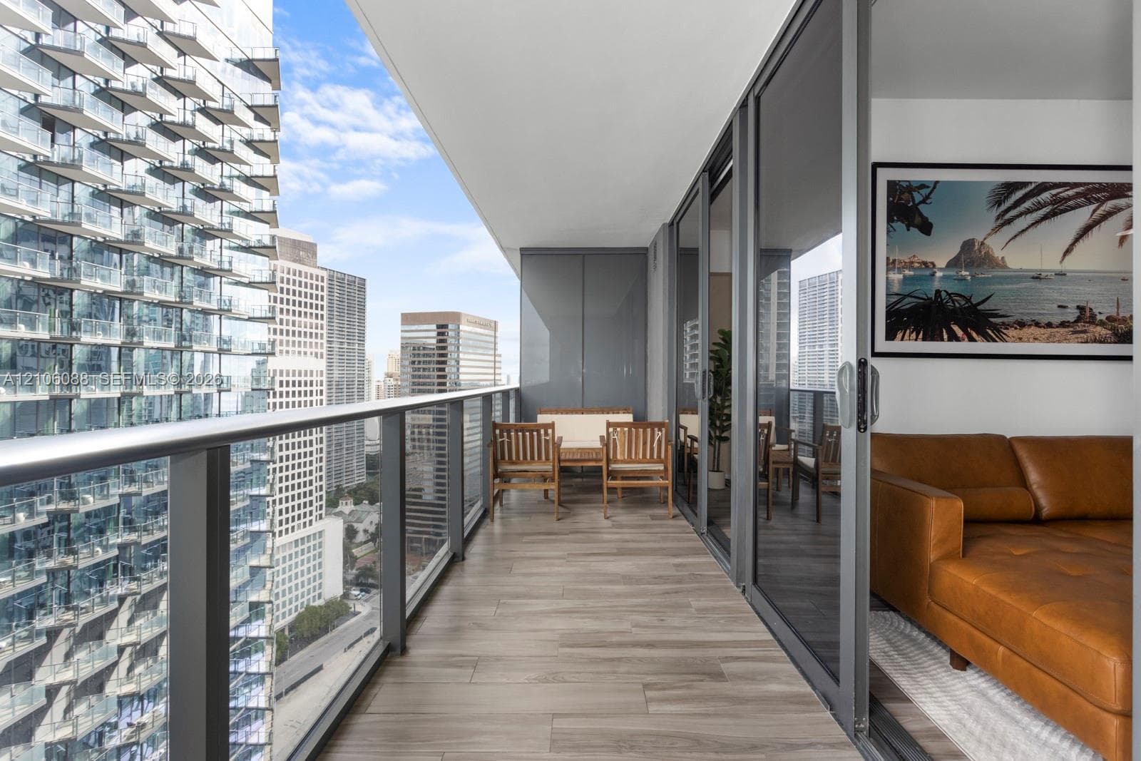Covered balcony featuring wood-finish flooring, full-height sliding glass doors, and a glass-paneled railing