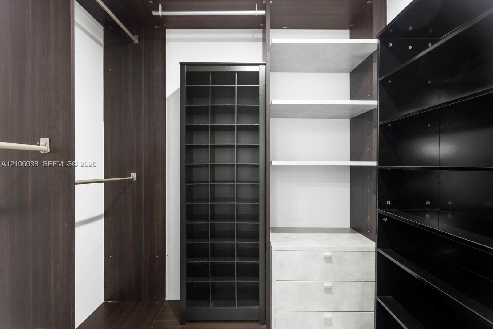 Custom storage system featuring dark wood-finish cabinetry, a built-in shoe rack, three integrated drawers with a stone-finish facade, open shelving, and metal garment rods