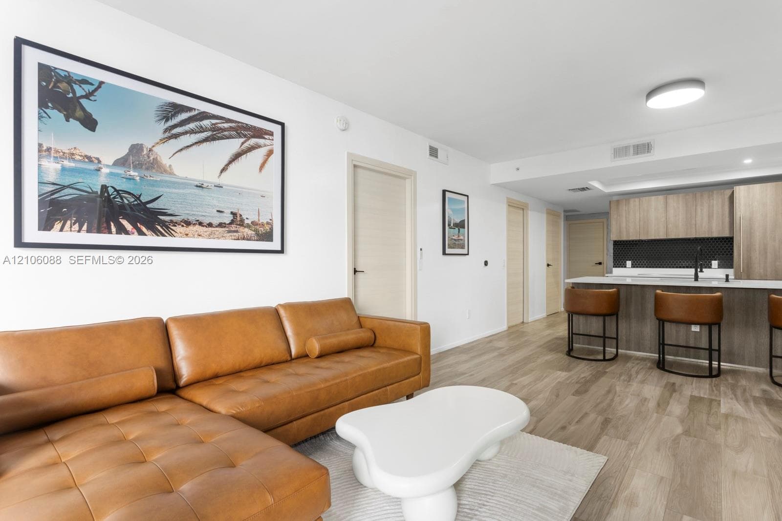 Open-concept interior featuring wood-finish flooring, recessed lighting, and a modern kitchen with wood-finish cabinetry, a contrasting hexagon tile backsplash, and a solid-surface breakfast bar