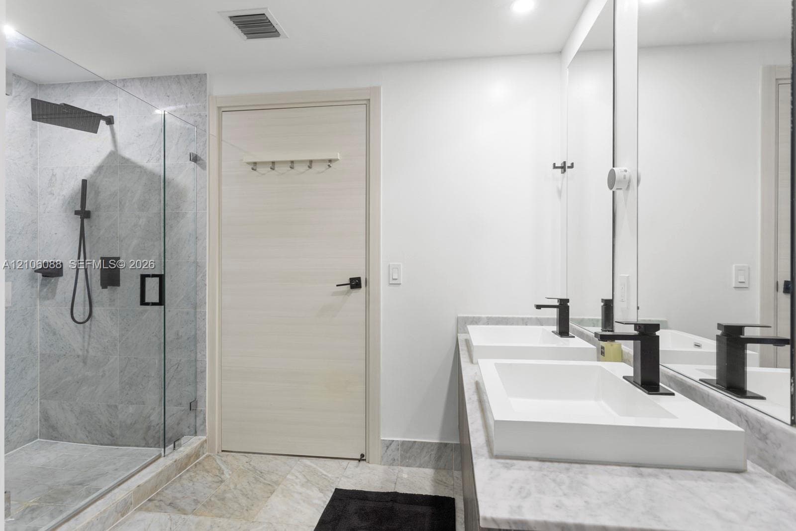 Dual-sink vanity with rectangular vessel basins, matte black plumbing fixtures, walk-in shower with stone-finish tile surround, frameless glass enclosure, and stone-finish flooring
