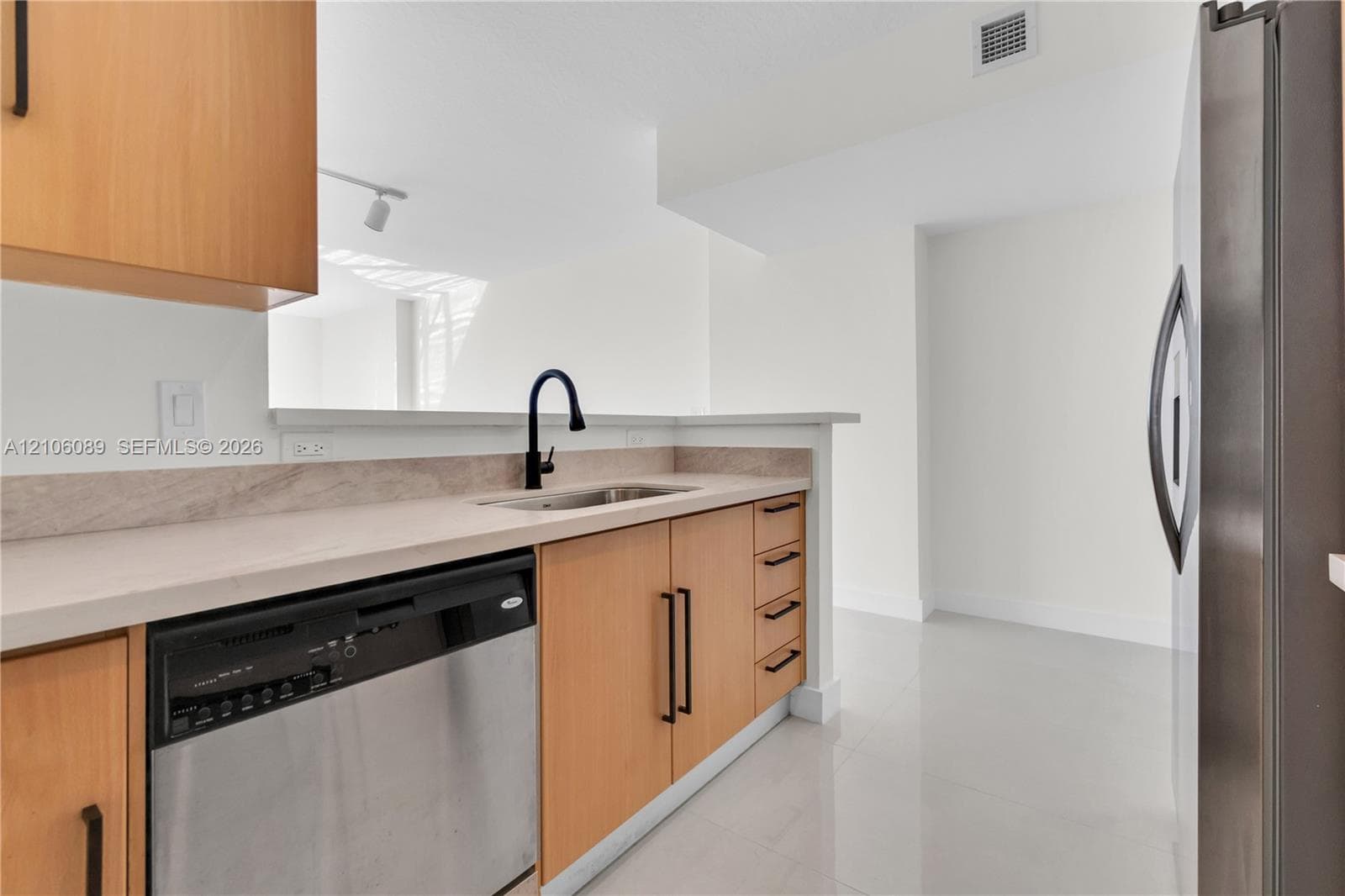 Kitchen featuring flat-panel wood cabinetry, light-toned countertops with matching backsplash, stainless steel dishwasher, matte black pull-down faucet, and polished tile flooring