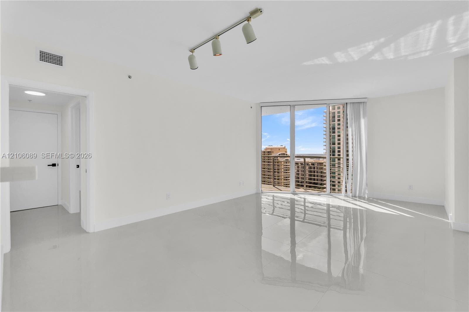 Living area featuring polished tile flooring, floor-to-ceiling glass panel doors, track lighting, and a metal-railing balcony