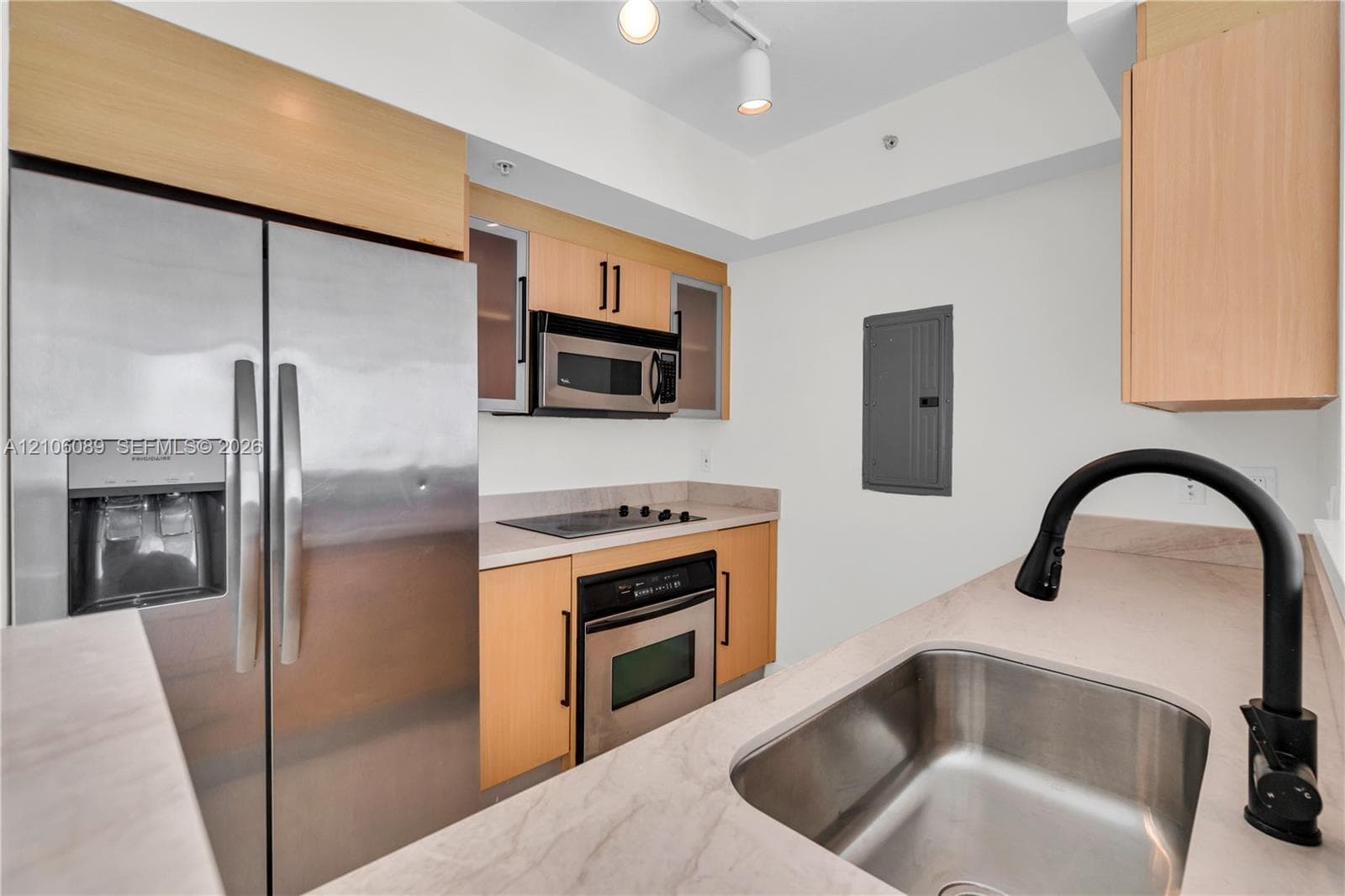 Kitchen featuring light wood-finish cabinetry, stainless steel appliances, solid-surface countertops, a stainless steel undermount sink, and a matte black high-arc faucet
