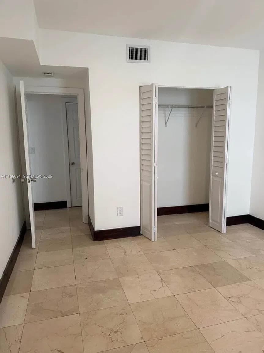 Neutral stone-tile flooring, louvered bi-fold closet doors, and dark wood-finish trim throughout