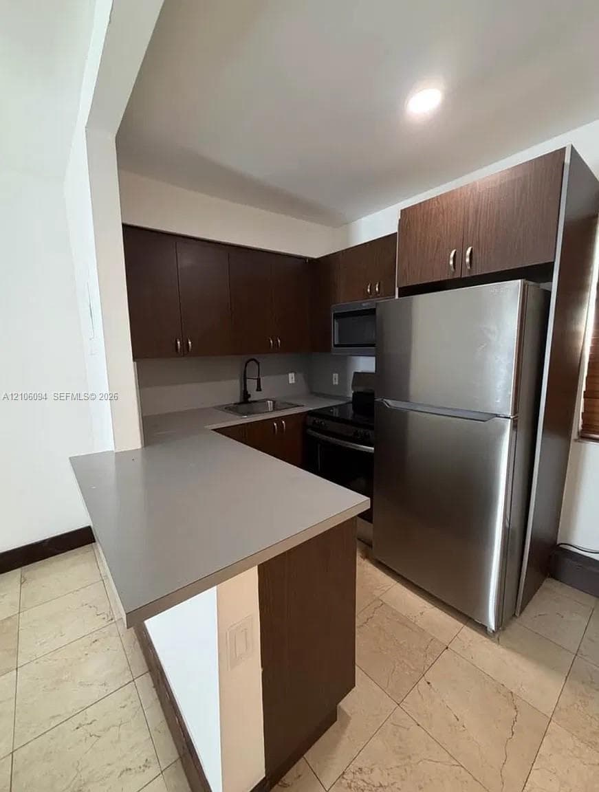 Kitchen featuring dark-finish cabinetry, solid surface countertops, stainless steel refrigerator, over-the-range microwave, and tile flooring
