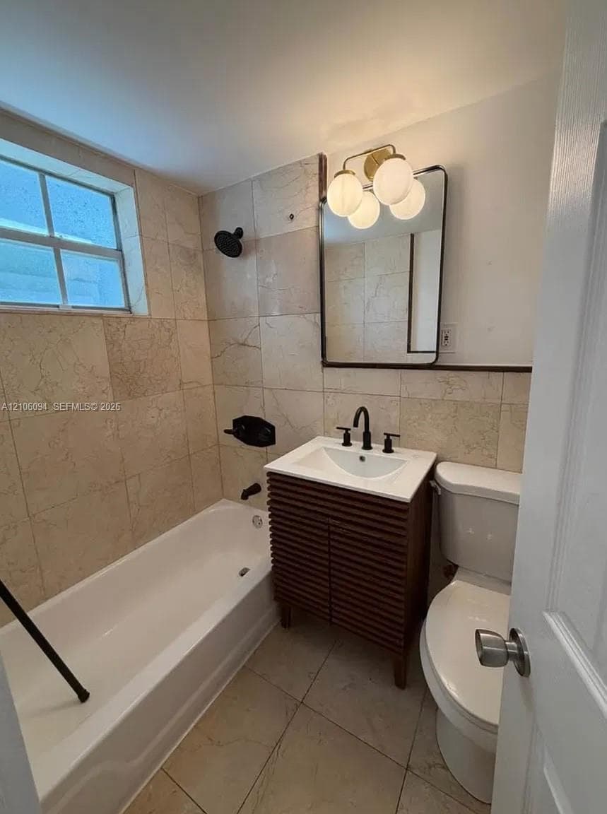Slatted wood-finish vanity with a rectangular sink, stone-tiled walls and flooring, matte black plumbing fixtures, and a multi-bulb vanity light