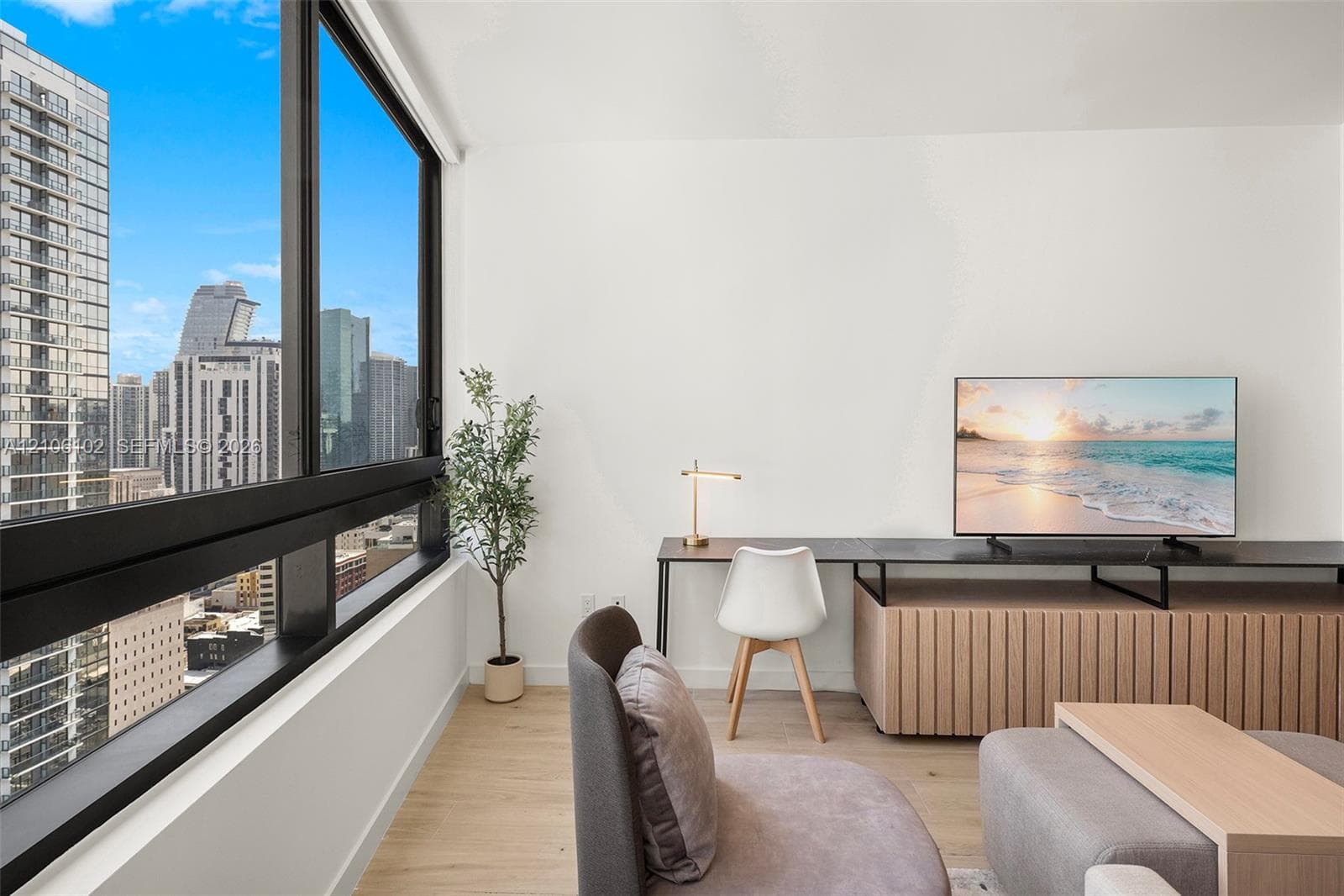 Floor-to-ceiling windows featuring panoramic urban scenery, light wood-finish flooring, and a custom built-in low-profile media console with fluted wood cabinetry