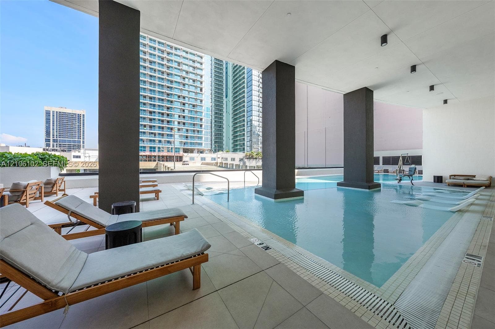 Covered swimming pool featuring large structural columns, light-toned tile decking, and recessed ceiling lighting