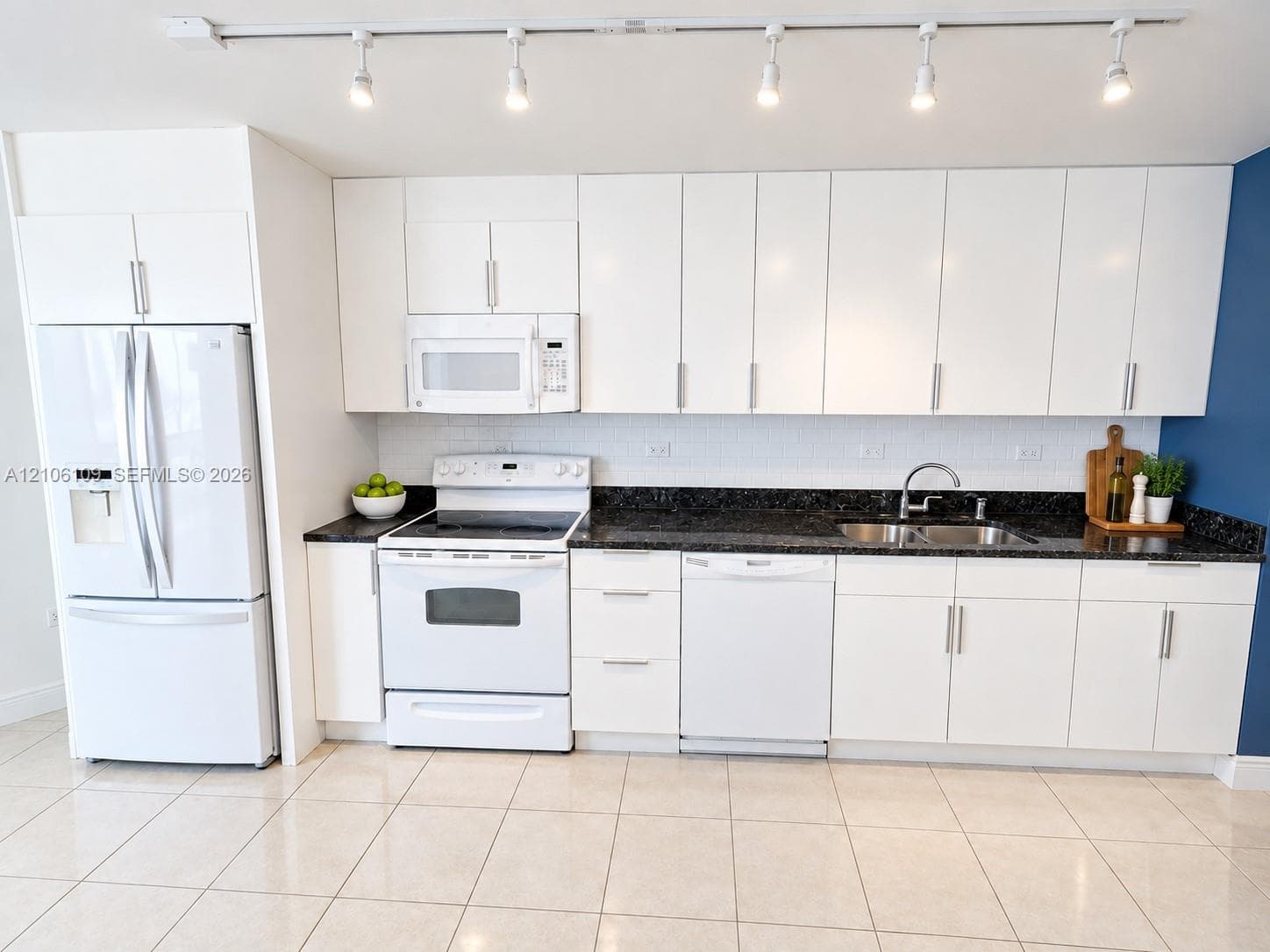 Kitchen featuring white cabinetry, dark stone countertops, tile flooring, integrated white appliances, and a ceiling-mounted track lighting system
