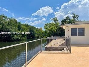 Waterfront patio featuring a concrete deck, chain-link fencing, and mature perimeter trees