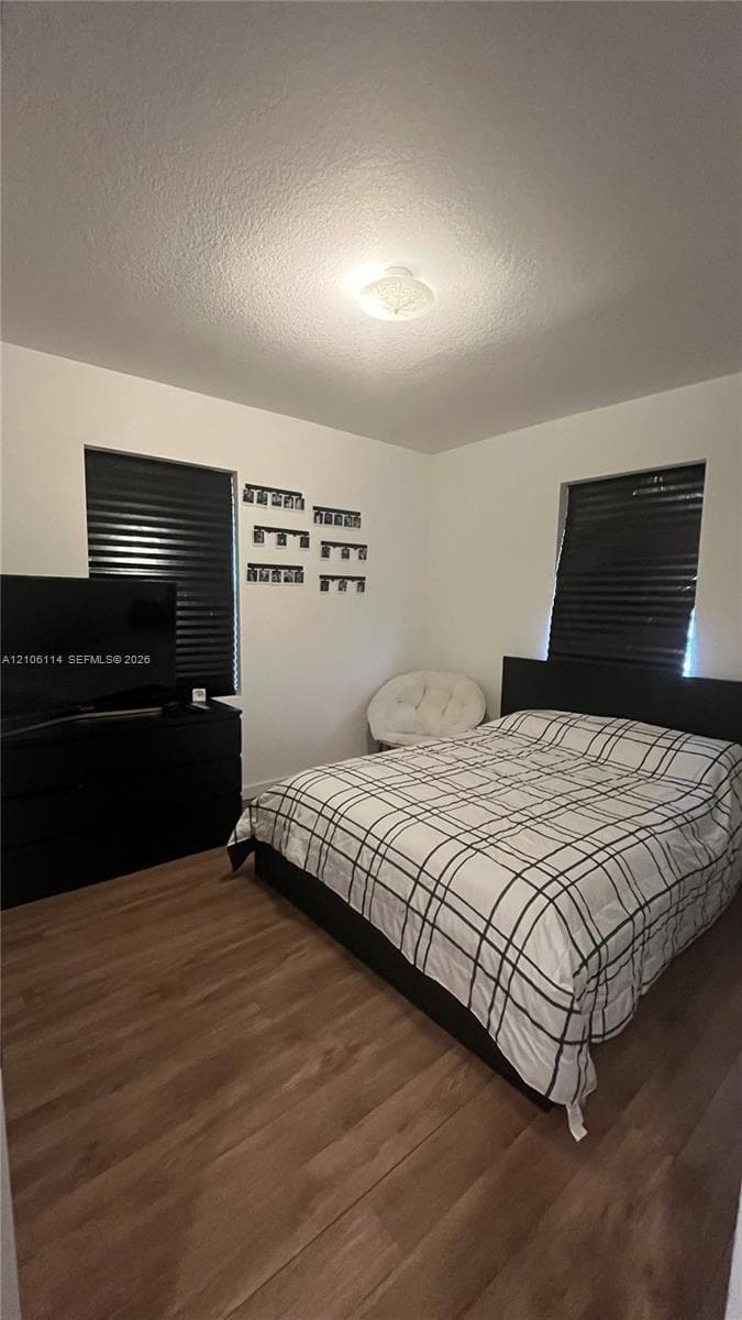 Room featuring wood-finish flooring, white walls, and two windows with black window treatments