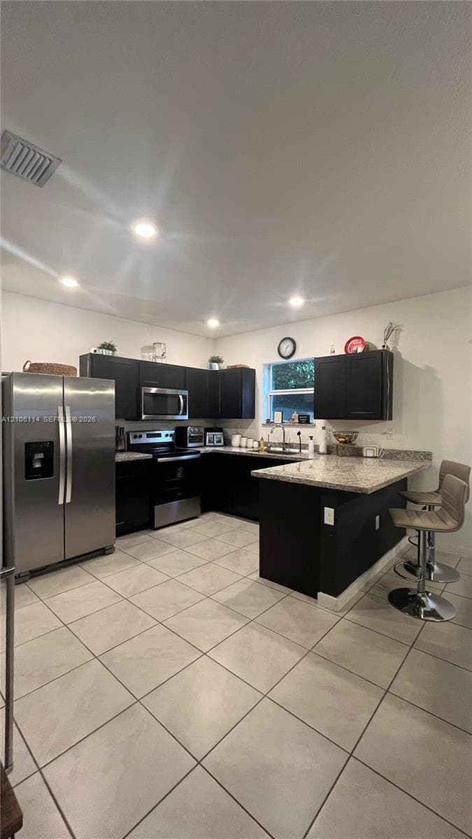 Kitchen featuring dark cabinetry, stone-finish countertops, stainless steel appliances, a breakfast bar, and tile flooring