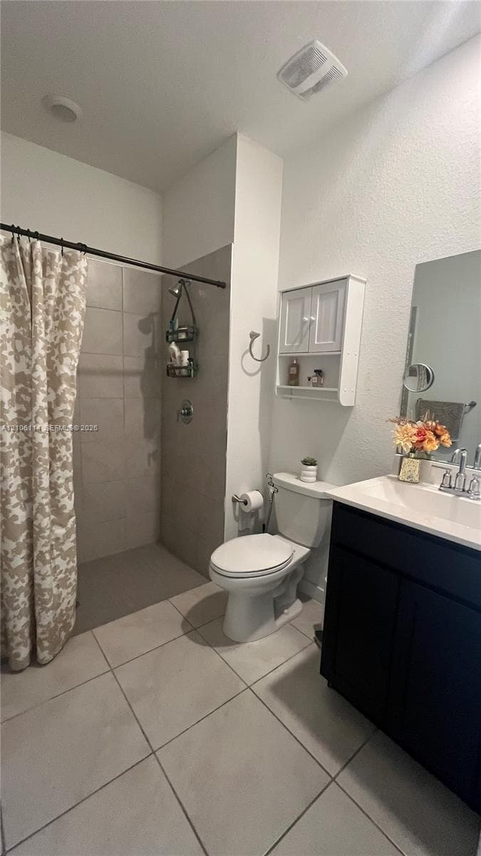 Bathroom featuring large-format tile flooring, dark cabinetry with a white countertop, walk-in shower with full-height neutral wall tile, and built-in wall cabinetry