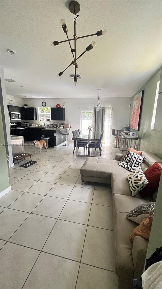 Open-concept interior featuring large-format tile flooring, modern multi-arm chandelier lighting, and a kitchen equipped with dark cabinetry