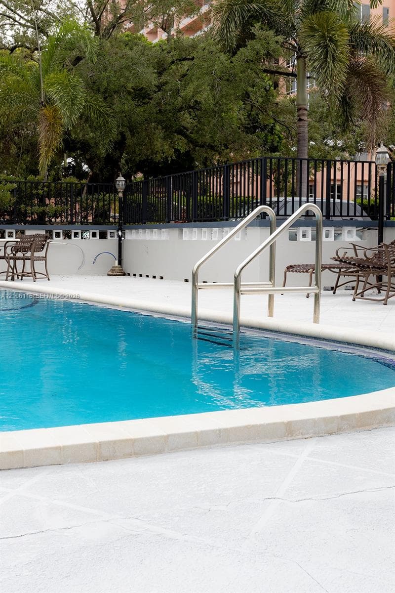 Swimming pool with light-colored concrete decking, metal handrail, perimeter black metal fencing, and decorative stone wall accents