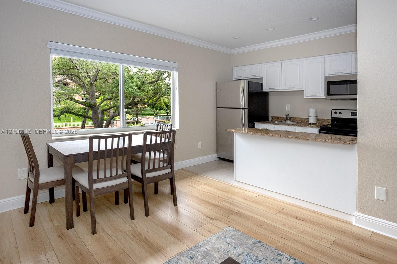 Kitchen featuring white cabinetry, stone-surface countertops, built-in microwave, and stainless steel refrigerator, complemented by wood-finish flooring and crown molding