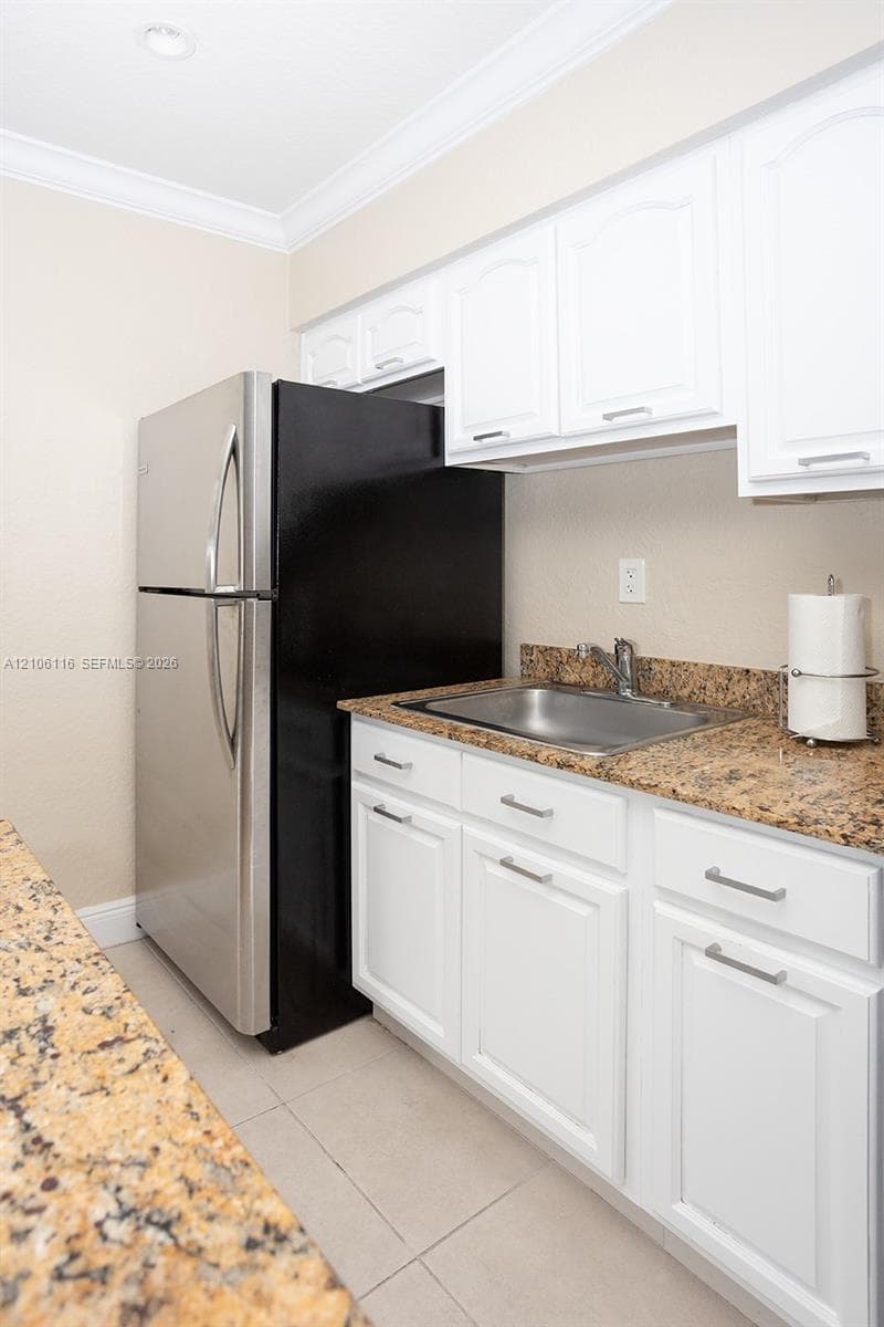 Kitchenette area featuring white shaker-style cabinetry, stone-surface countertops, stainless steel drop-in sink with faucet, and stainless steel refrigerator