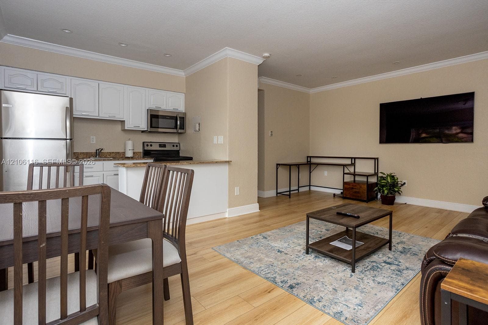 Kitchen area featuring white cabinetry, stone-finish countertops, stainless steel appliances, and wood-finish flooring with crown molding
