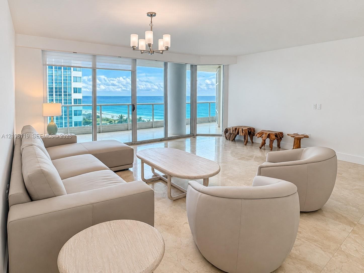 Floor-to-ceiling glass sliders, stone tile flooring, circular flush-mount ceiling light, and coastal ocean horizon