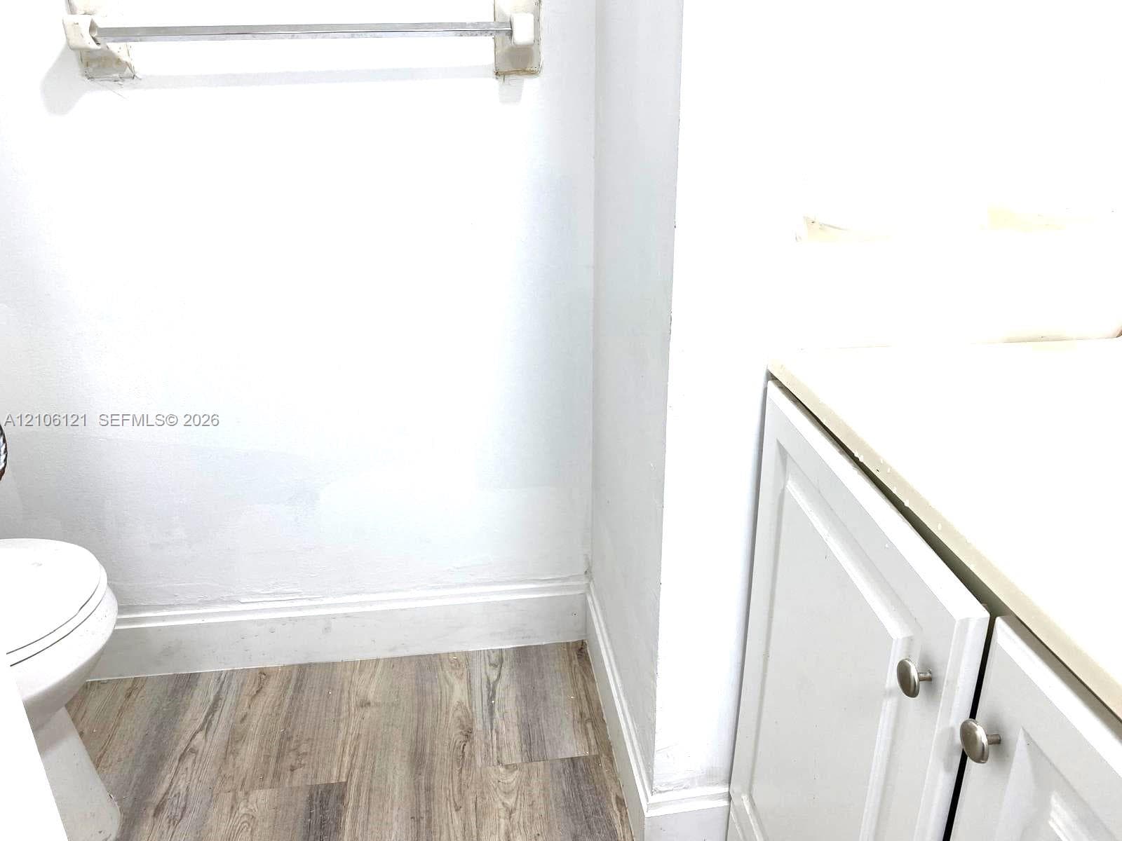 Bathroom featuring wood-finish flooring, white cabinetry with round metallic hardware, and a solid-surface countertop