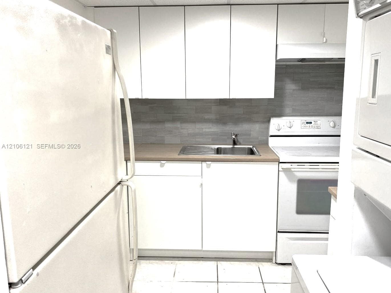 White cabinetry, neutral-toned backsplash, built-in range with overhead vent, stainless steel sink, and tile flooring