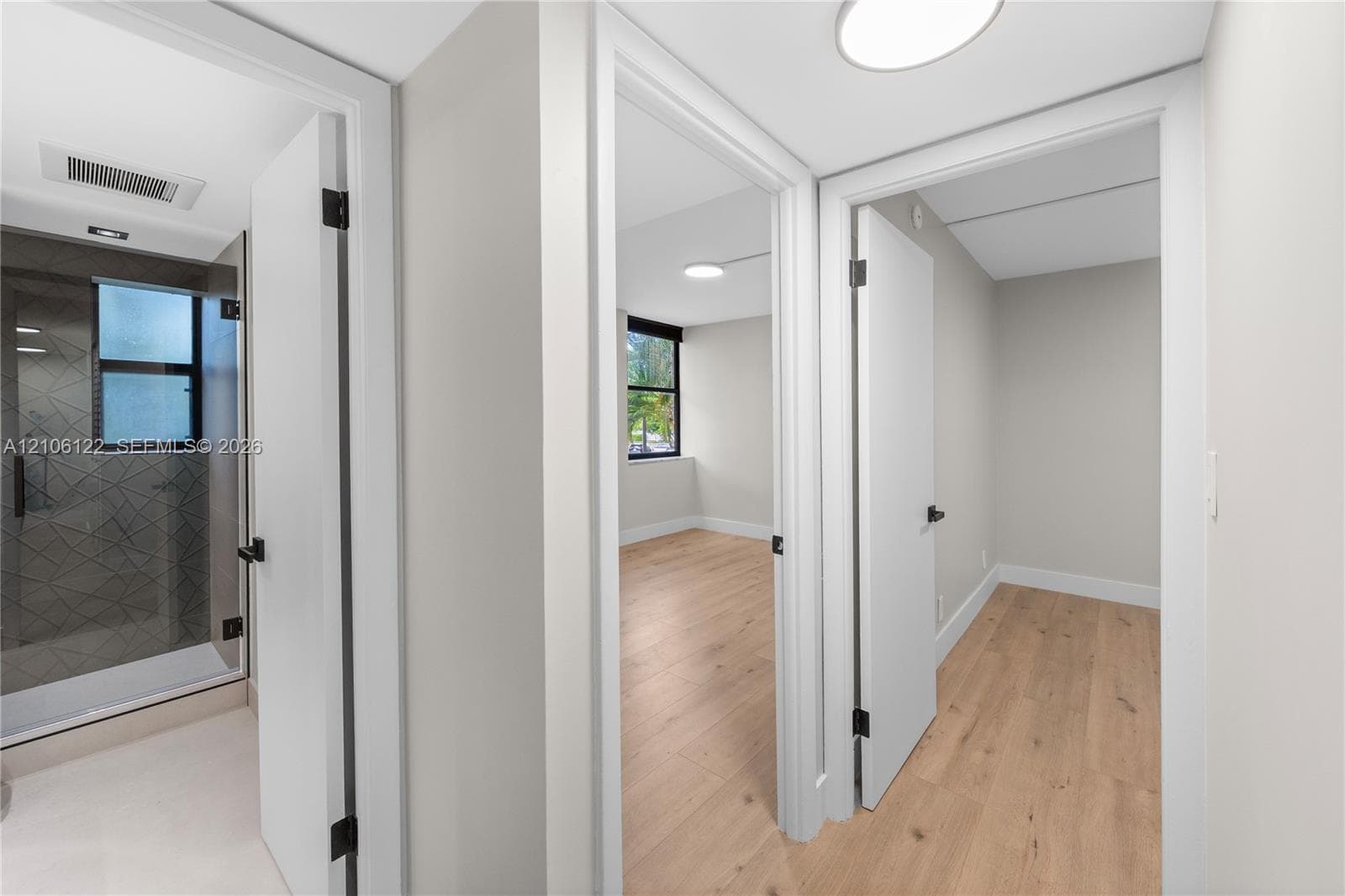 Hallway featuring wood-finish flooring, white doors with matte black hardware, and a walk-in shower with geometric-patterned tile walls