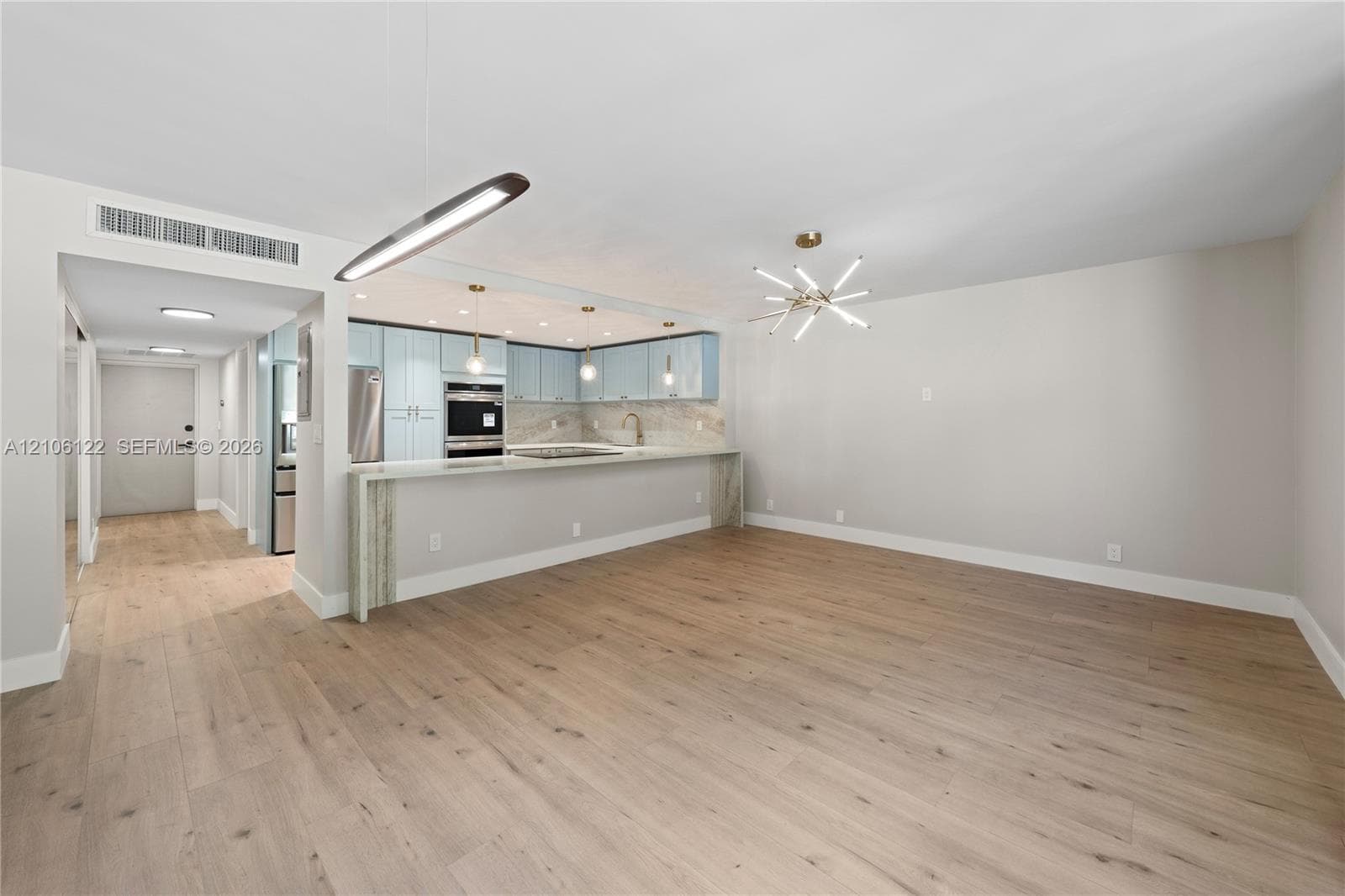 Kitchen featuring light blue cabinetry, stone countertops, integrated stainless steel appliances, wood-finish flooring, and multi-light pendant fixtures