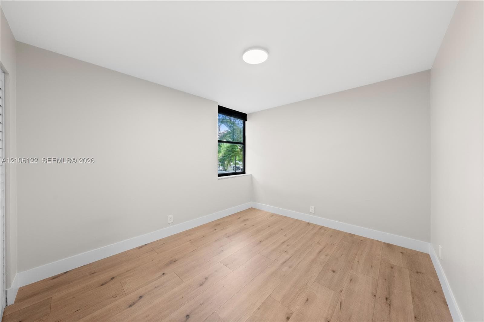 Neutral interior space featuring wood-finish flooring, crisp white wall paint, and a single window with a black frame