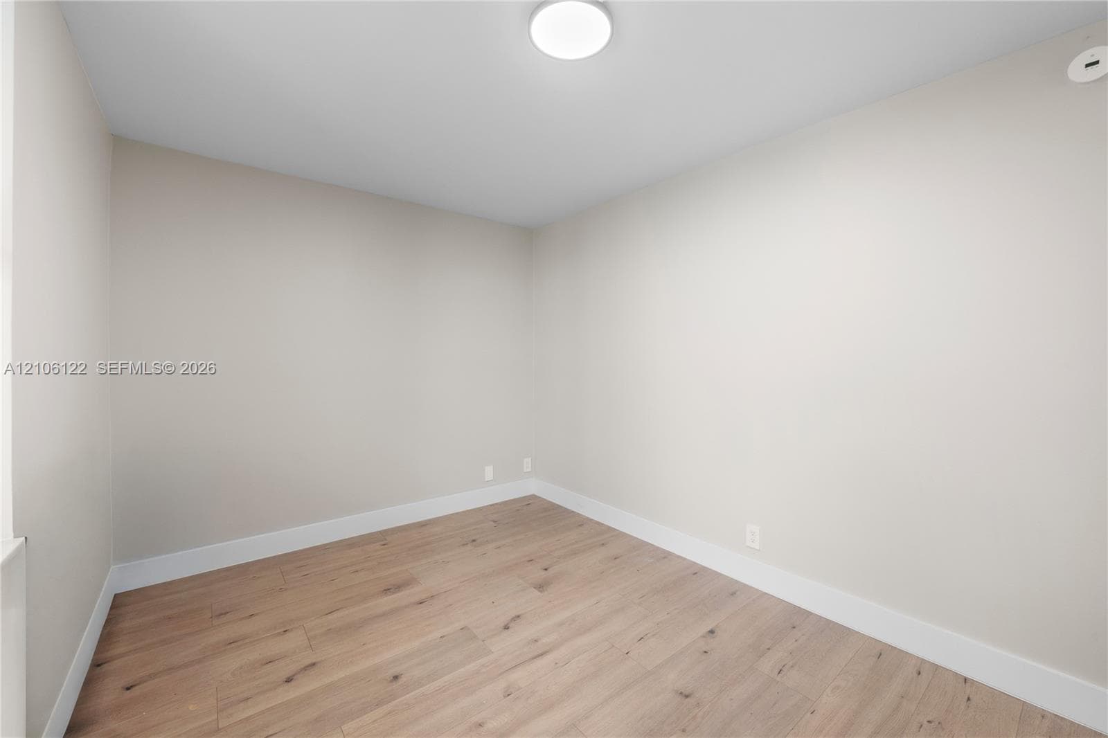 Neutral-toned interior space featuring light wood-finish flooring, smooth wall finishes, and a flush-mount ceiling light fixture