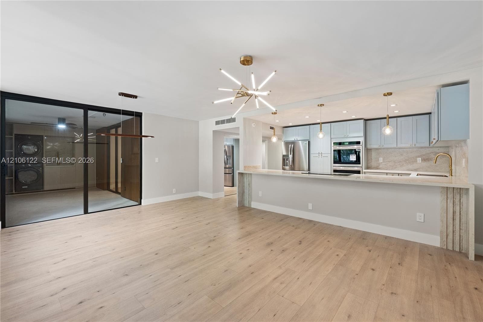 Kitchen featuring custom cabinetry, light-toned stone-finish countertops, stainless steel built-in appliances, a modern multi-arm chandelier, and wide-plank wood-finish flooring