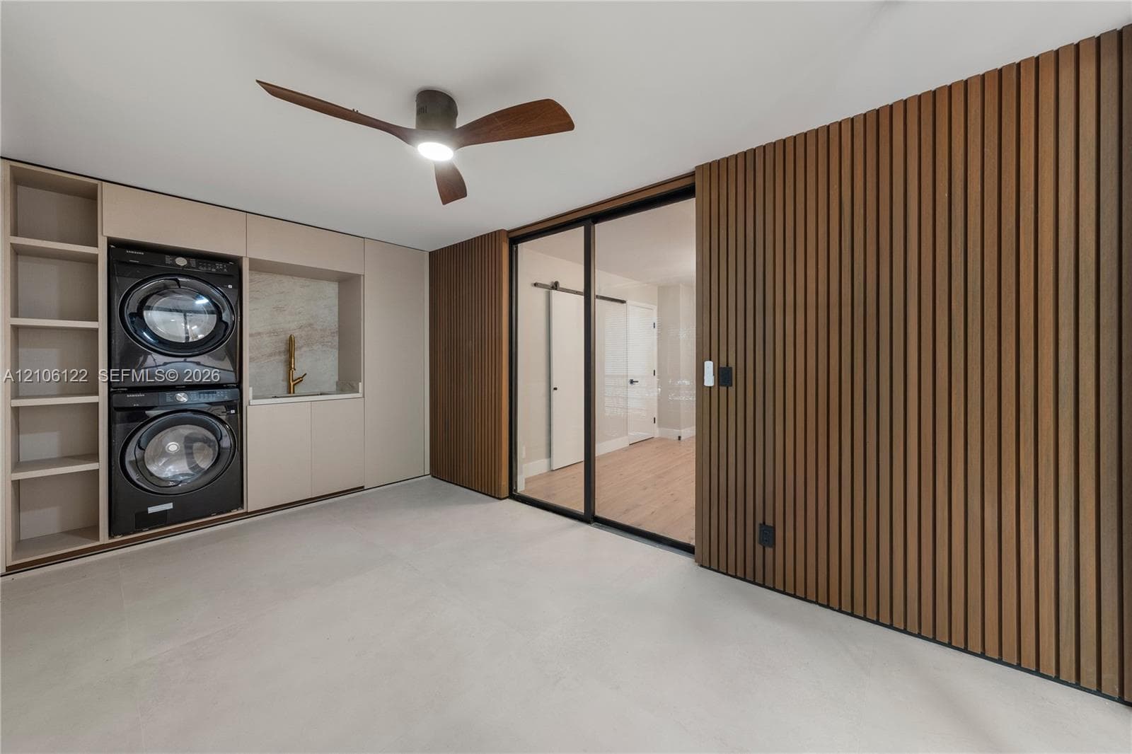Custom built-in cabinetry featuring integrated laundry appliances, wood-slat accent wall, stone-surround utility sink, sliding glass door with black frame, and wood-finish ceiling fan