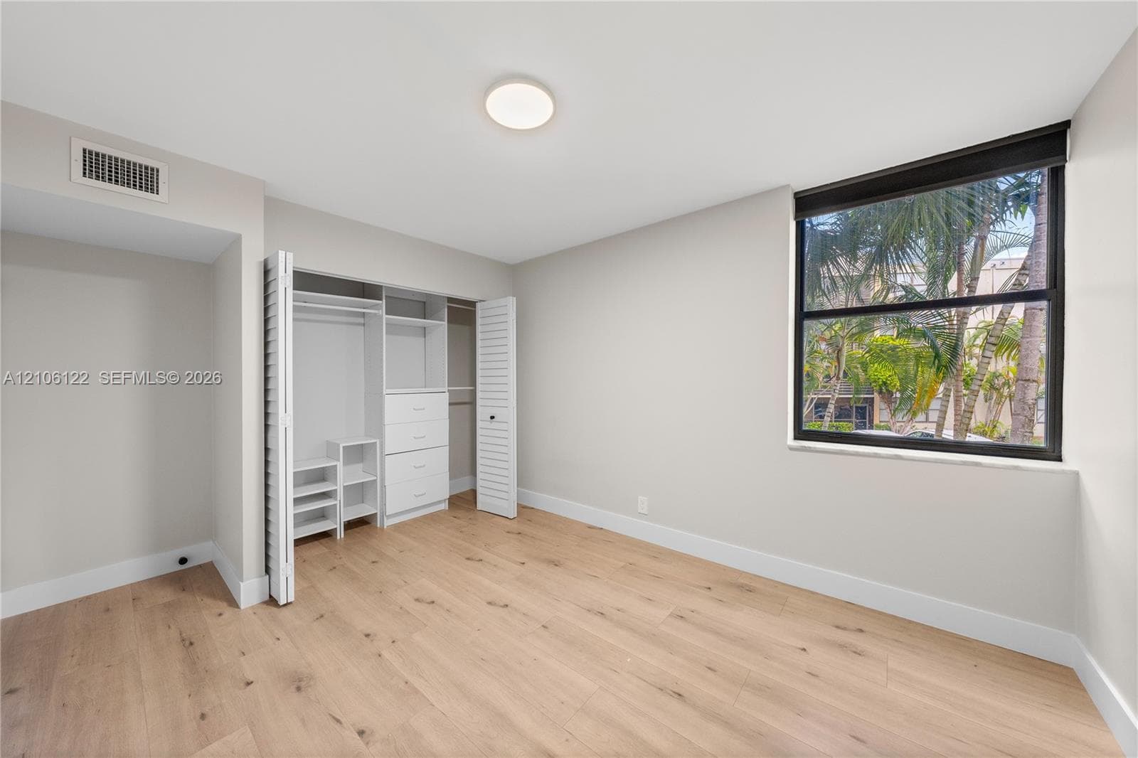 Room featuring wood-finish flooring, a large window with black framing, and a built-in closet system with integrated shelving and drawers