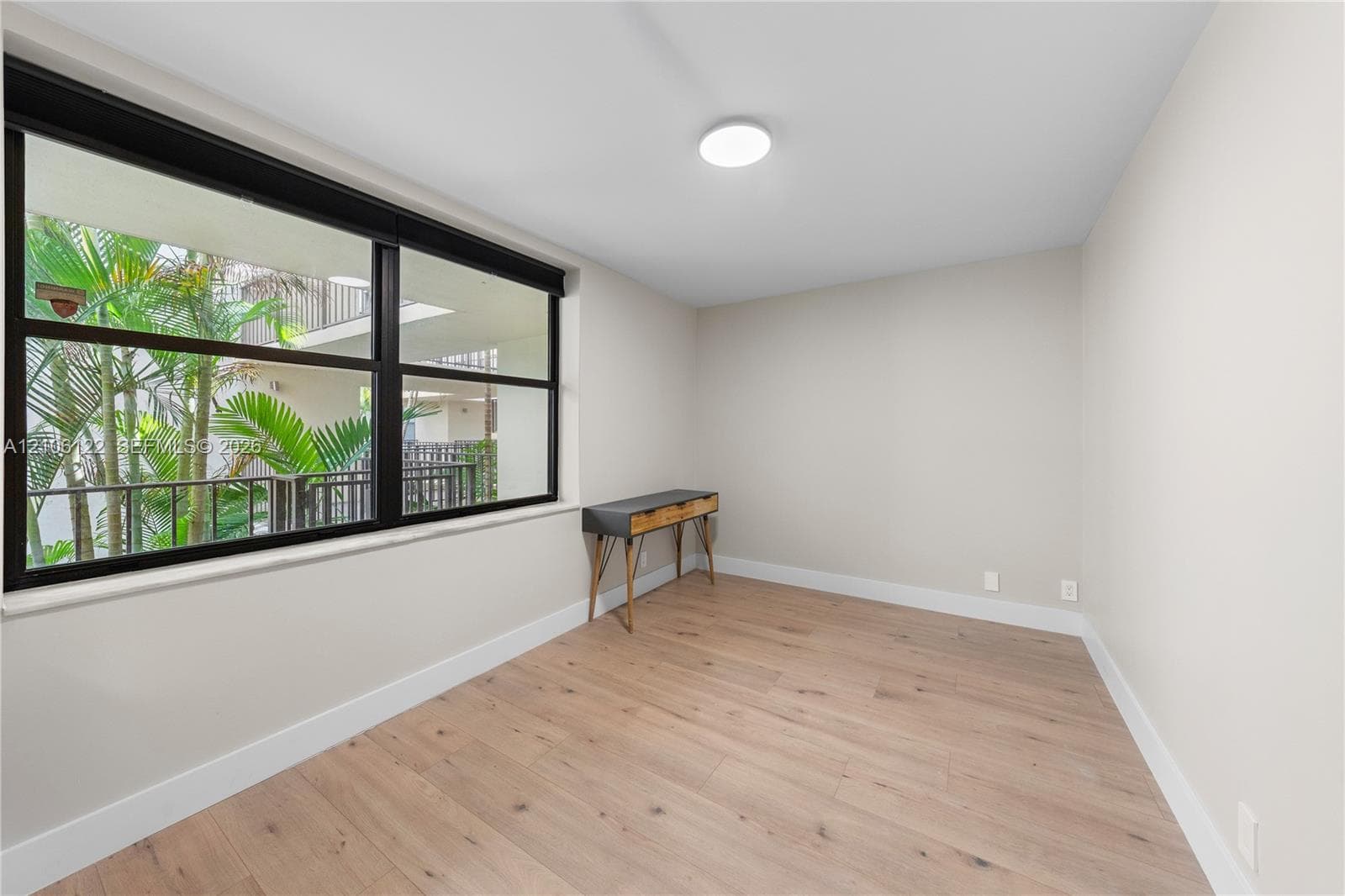 Interior space featuring wood-finish flooring, neutral wall paint, and a large window with black framing