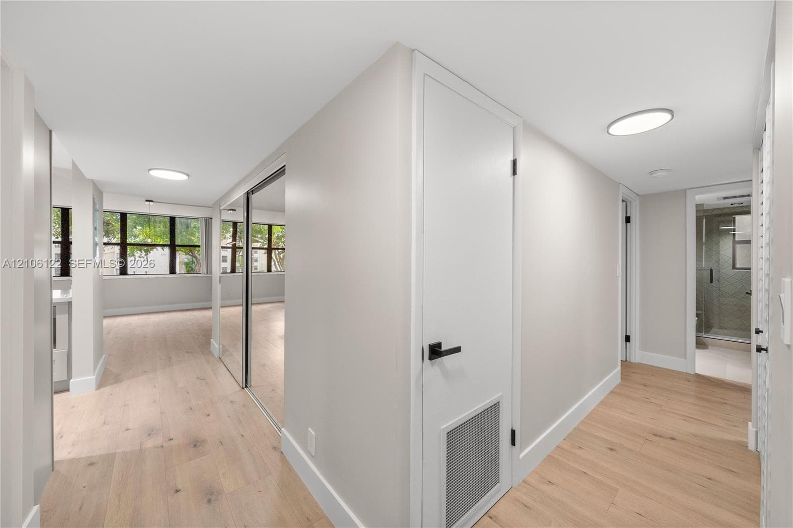 Interior space featuring wood-finish flooring, floor-to-ceiling mirrored closet doors, flush-mount circular lighting, and matte black door hardware