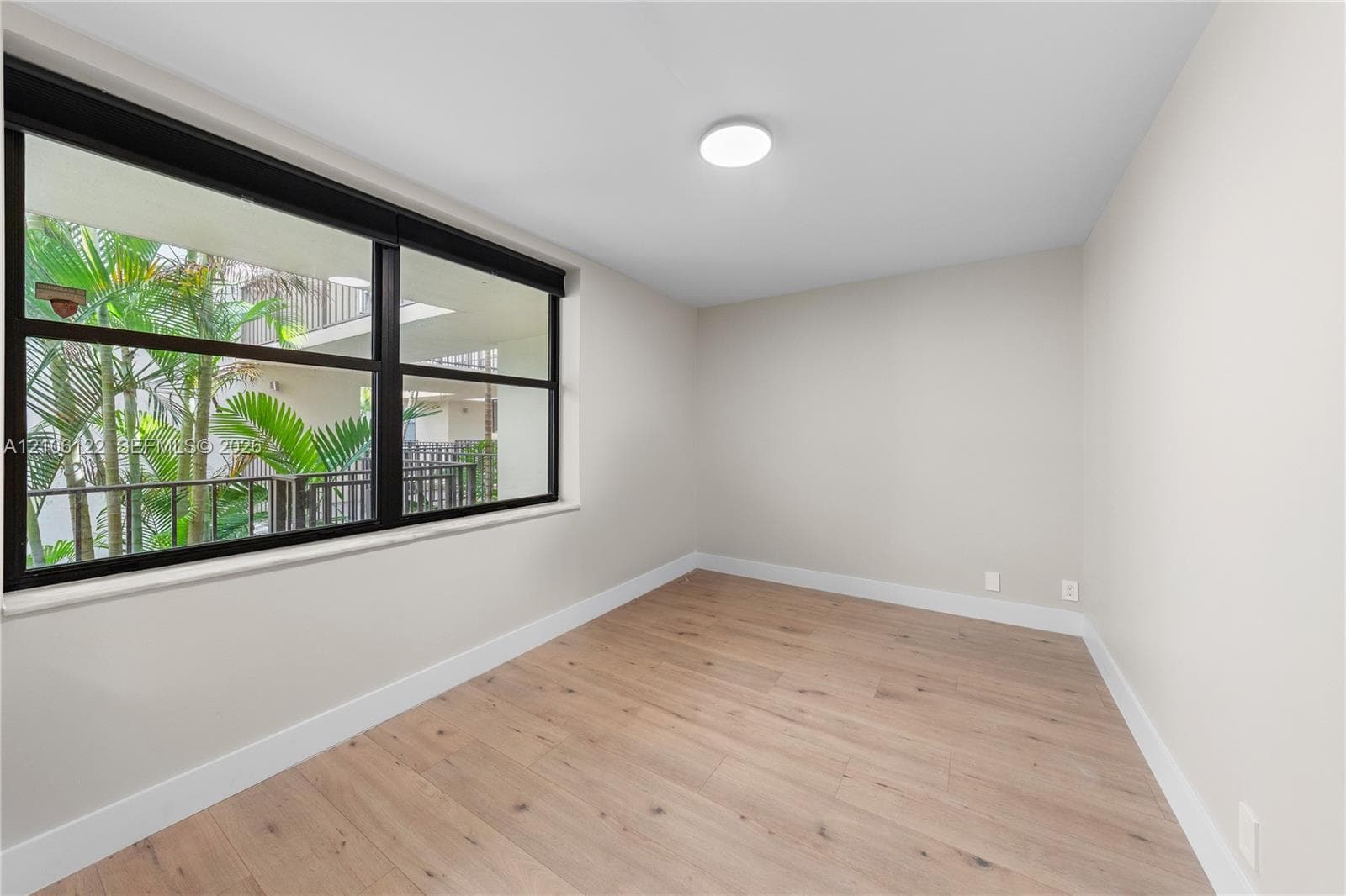 Interior room featuring wood-finish flooring, neutral wall paint, and a large window with a black frame