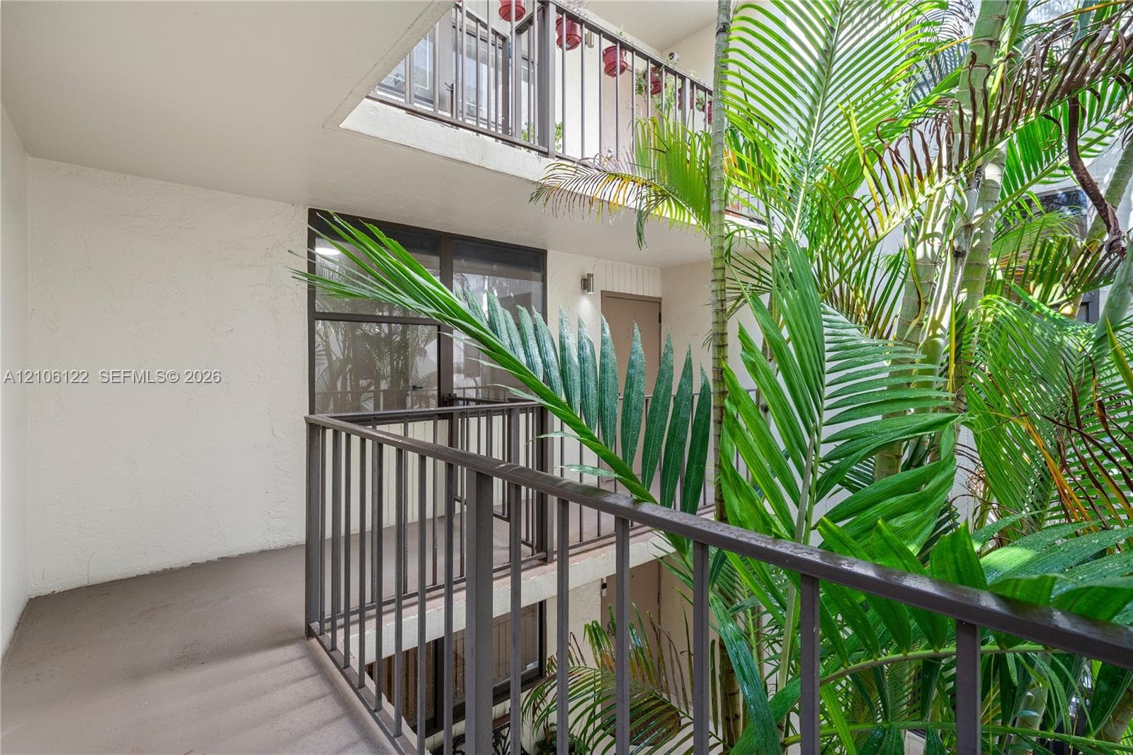 Covered exterior walkway featuring metal railings, neutral wall finishes, and tropical foliage