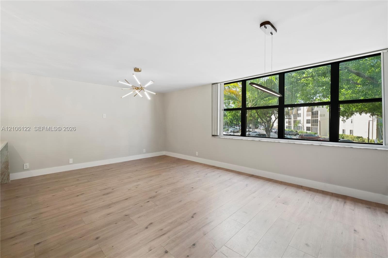 Expansive room featuring wood-finish flooring, large windows with black frames, a multi-arm sputnik chandelier, and a contemporary linear pendant light