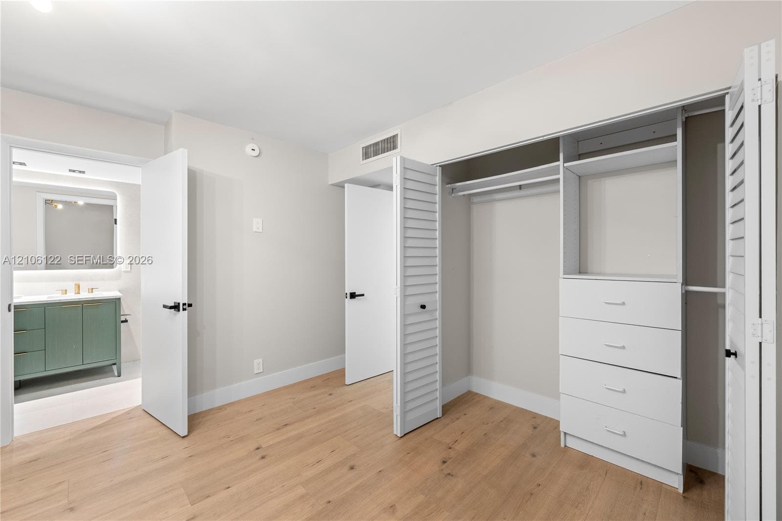 Room featuring wood-finish flooring, built-in closet system with integrated shelving and drawers, louvered closet doors, and solid-core interior doors with matte black hardware